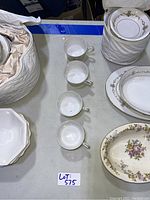Multiple white tea cups lined up with stacked plates showing floral and gold trim patterns