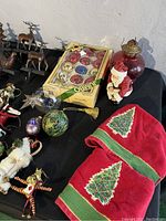 Photo of assorted Christmas decorations including glass ornaments, figurines, fabric tree skirts, and metallic figurines on a black surface.