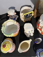 Six ceramic cookie jars and containers in various whimsical shapes and colors on black surface, including a bear chef cookie jar and dessert-shaped jar.
