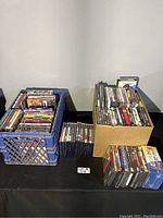 Overview photo showing two containers filled with DVDs and PS2 game cases arranged on a table.