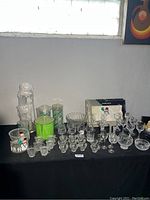 Wide view of glassware on black cloth including cordial glasses, bowls, frames and green Lucite item