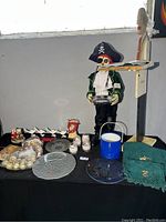 Photo showing pirate skeleton figurine holding a tray, clear glass plates, Christmas ornaments including silver and gold balls, candles, blue enamel bucket, and green cloth napkins.