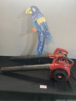 Side view showing red Toro and Homelite leaf blowers with a colorful blue bird lawn decoration behind.