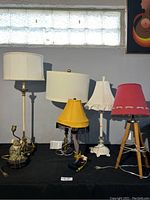 Five modern style lamps displayed on black cloth, showing variety of designs and lampshades