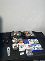 Full lot overview showing games, game accessories, DVDs, and carrying case arranged on black cloth.