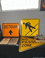 Three large vintage street signs including Detour, pedestrian warning, and No Passing Zone plus two smaller parking signs on a black cloth surface near a window