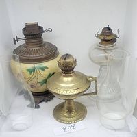 Photo showing all three oil lamps and two glass chimneys grouped together on a white surface.