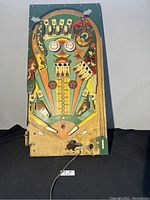 Full view of the wooden playfield with colorful artwork and pinball components visible, set vertically.