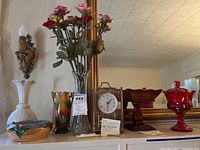 Overview showing porcelain vase, glass vase with porcelain roses, Kundo gold-tone mantle clock, Japanese bowl, ruby red crown dish on wooden holder
