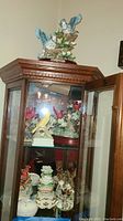 Full view of display cabinet containing multiple bird figurines and music boxes including red birds, delicate floral decorations, and porcelain pieces.