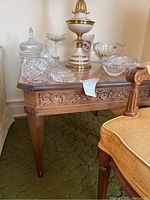 Full view of the wood end table showing carved apron and tapered leg detail with some glassware on top (not included)