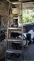 Full view of the 6 foot metal ladder with visible paint marks and side writing, shown in a garage setting with other items in background.