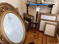 Overview of all eleven frames leaning against wall and on floor including large ornate oval frame and other rectangular frames
