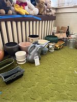 Assorted ceramic planters and decorative items arranged on green carpet with stuffed animals in background.