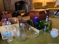 Overview photo of assorted glassware on a table including vases, small green tumblers, stemmed glasses, and a wooden box in background.