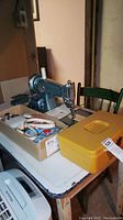 Wide angled photo showing vintage Kingston sewing machine on table with accompanying sewing notions and yellow sewing box.