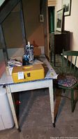 Vintage table and chair with sewing machine and yellow case placed on table, showing table legs and chair cushion.