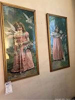 Two framed vertical prints displayed side by side on a wall, depicting Victorian children in pink dresses with birds and rabbits in a green natural background.