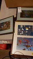 Photo showing three framed wall art pieces, includes two nature landscape prints and one dual bird image print with flowers in a bamboo-style frame.