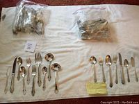 Two separate silverplate flatware sets spread on white towel with many utensil types displayed including serving spoons, knives, forks, ladles, butter knives.