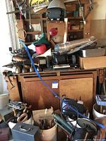 Photo showing stacked toolboxes, vintage tools, oil cans, motors, and miscellaneous workshop equipment piled on a wooden cabinet