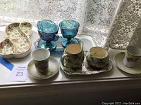 Lot displayed showing carnival glass cream and sugar set, two blue carnival glass goblets, German hand painted tea cups and ceramic vase on a lace tablecloth.