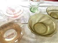 Three amber depression glass bowls, pink glass cake dish, and twelve inch green glass vase on white cloth.