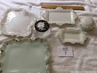 Photo showing two dresser sets, four trays of varying sizes and one trinket box, all with scalloped edges and floral embossing, plus a glass hair catcher with metal decorative lid.