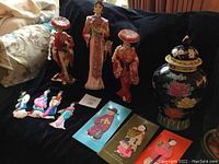 Three tall dolls (two with hats), four smaller fabric dolls in front, three collectible mythology cards, and floral urn at right side.