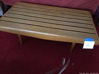 Full view of the medium colored oak slat top table with simple tapered legs on red carpet, highlighting the rectangular slatted top and overall condition.