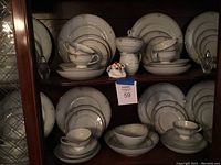 Full view showing multiple stacked place settings including various plates, bowls, cups, saucers, as well as cream and sugar set positioned near center, and gravy and vegetable bowls on right.