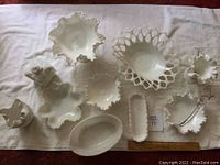 Full view of milk glass items on a white fabric background including candy dishes, vases, and serving pieces.