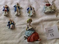 Top-down view of six figurines including couples and seated woman in colorful dress with book