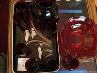 Red glass pitcher, six red glasses, decorative red glass bowl, red glass vase arranged on a black plastic tray with floral design