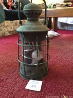 Front view of green metal ship lantern sitting on carpet with protective cage and vented top.