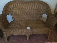 Full view of the tan wicker love seat showing overall shape and condition.