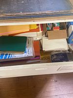 Photo showing a drawer containing notebook paper packs, colored construction paper, file cards, and boxed materials.