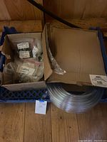 Box containing assorted washers and screws next to a roll of clear vinyl tubing on a crate.