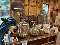 Photo showing silver glass pumpkins, a metal birdcage, pineapple decor and sea shells arranged on a wooden table.