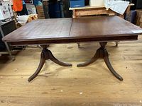 Front view of the wooden dining table showing double pedestal legs and tabletop with slight wear and built-in leaf.