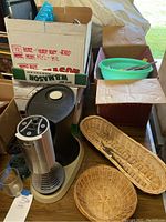 Flavia Fusion drink station machine with assorted mugs and woven baskets packed in boxes on a table.
