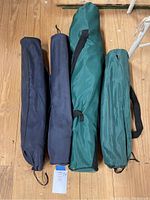 Four carry bags for foldable chairs in blue and green colors, standing upright on wooden floor