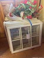 Photo showing stacked white framed glass pane windows with a hanging faux flower arrangement on top.