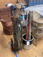 Photo showing two leather-like golf bags on a metal handcart with multiple golf clubs inside the bags, set on wooden floor.