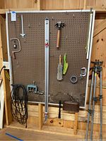 Full view of mounted pegboard with various tools including hammer, saw, brushes, measuring tape, dustpan, level, and hooks on the wall.
