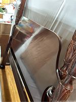 Close-up of headboard's dark polished wood surface showing its smooth finish and carved post detail.