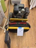 Top-down view showing the main engine, wheels, attached hose coiled around the yellow frame and spray wand laying beside it.