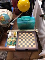 Photo showing a small globe, yellow planetarium model, turquoise plastic box, Yamaha soprano recorder bag, and a wooden foldable game board for multiple games.