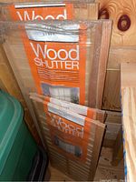 View of three pairs of wood shutters in original packaging stacked together. Labels showing sizes 14x32 and 14x44.