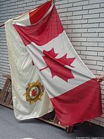 Two Canadian flags, one national and one Armed Forces, draped against a brick wall showing red and white colors and emblem on Armed Forces flag.